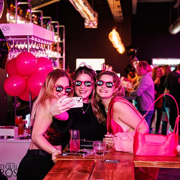 3 girls taking a selfie in front of the Tequila trolley on a night out at BOOM Battle Bar. All of them are wearing BOOM dress-up sunglasses