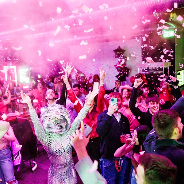 Large party scene at BOOM Battle Bar. A confetti canon has exploded above a crowd of party goers.